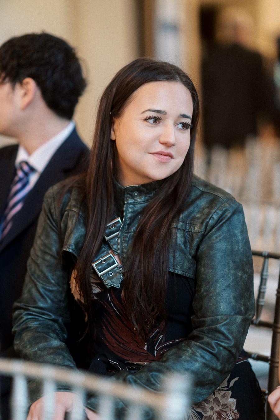 Woman in a green leather jacket seated beside her partner during an engagement photoshoot