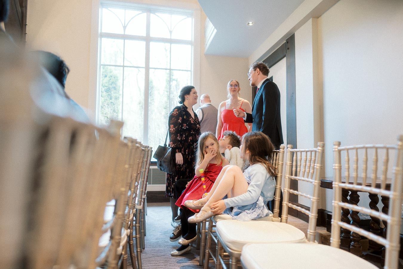 Guests and children gather between rows of chairs in a bright indoor event space.