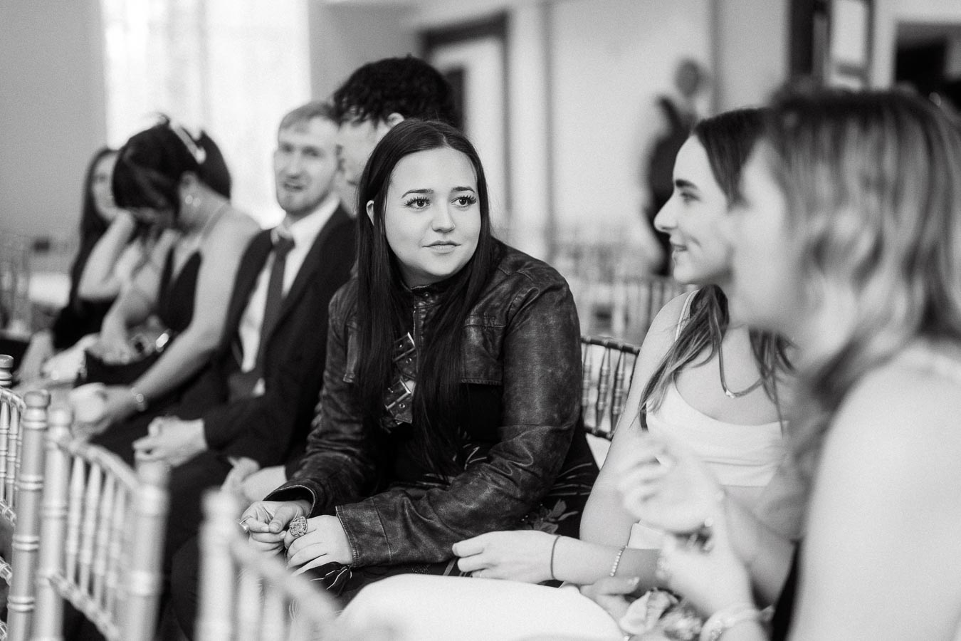 Guests seated in a row of chairs talking during an indoor gathering