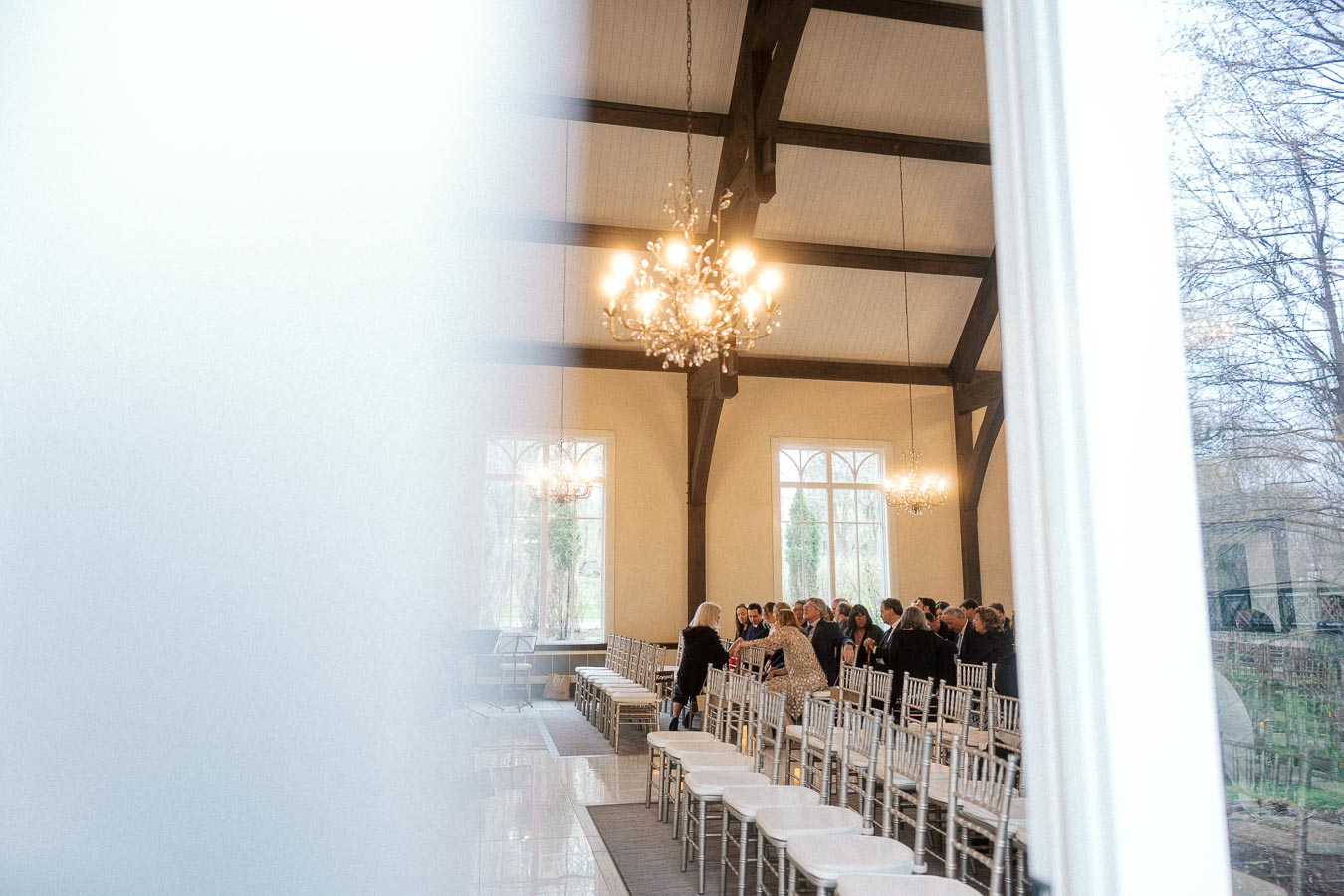 Guests seated in a bright ceremony hall with chandeliers and rows of white chairs
