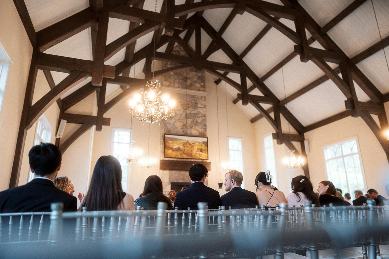 Guests seated inside a chapel with exposed wooden beams and chandeliers.