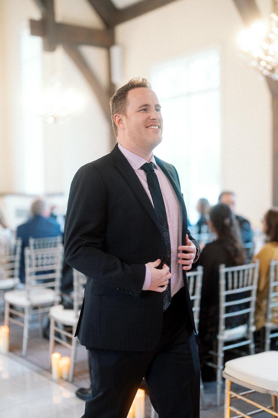 Smiling man in a dark suit standing inside a formal ceremony space