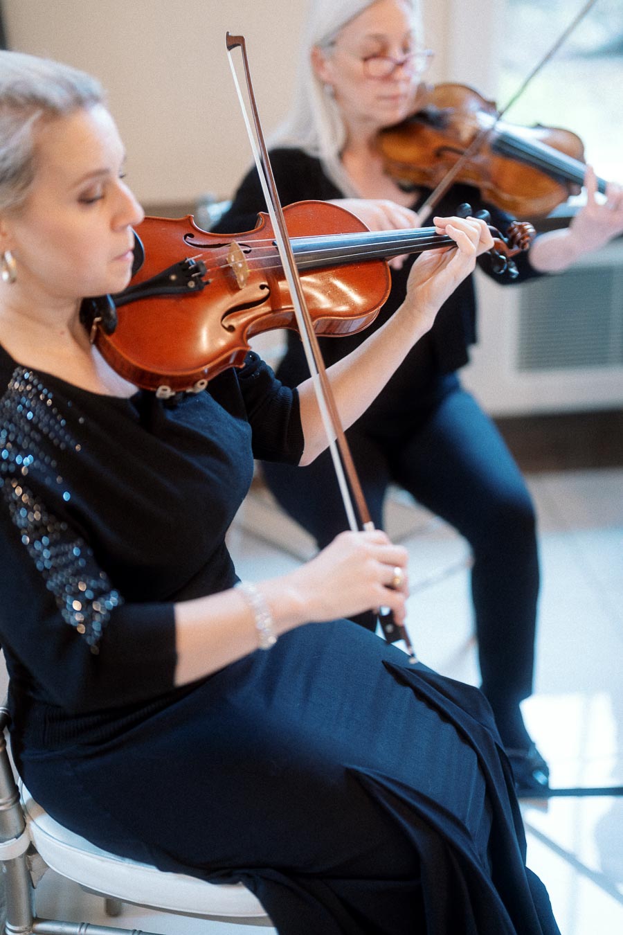 Two seated violinists performing indoors in black concert attire.