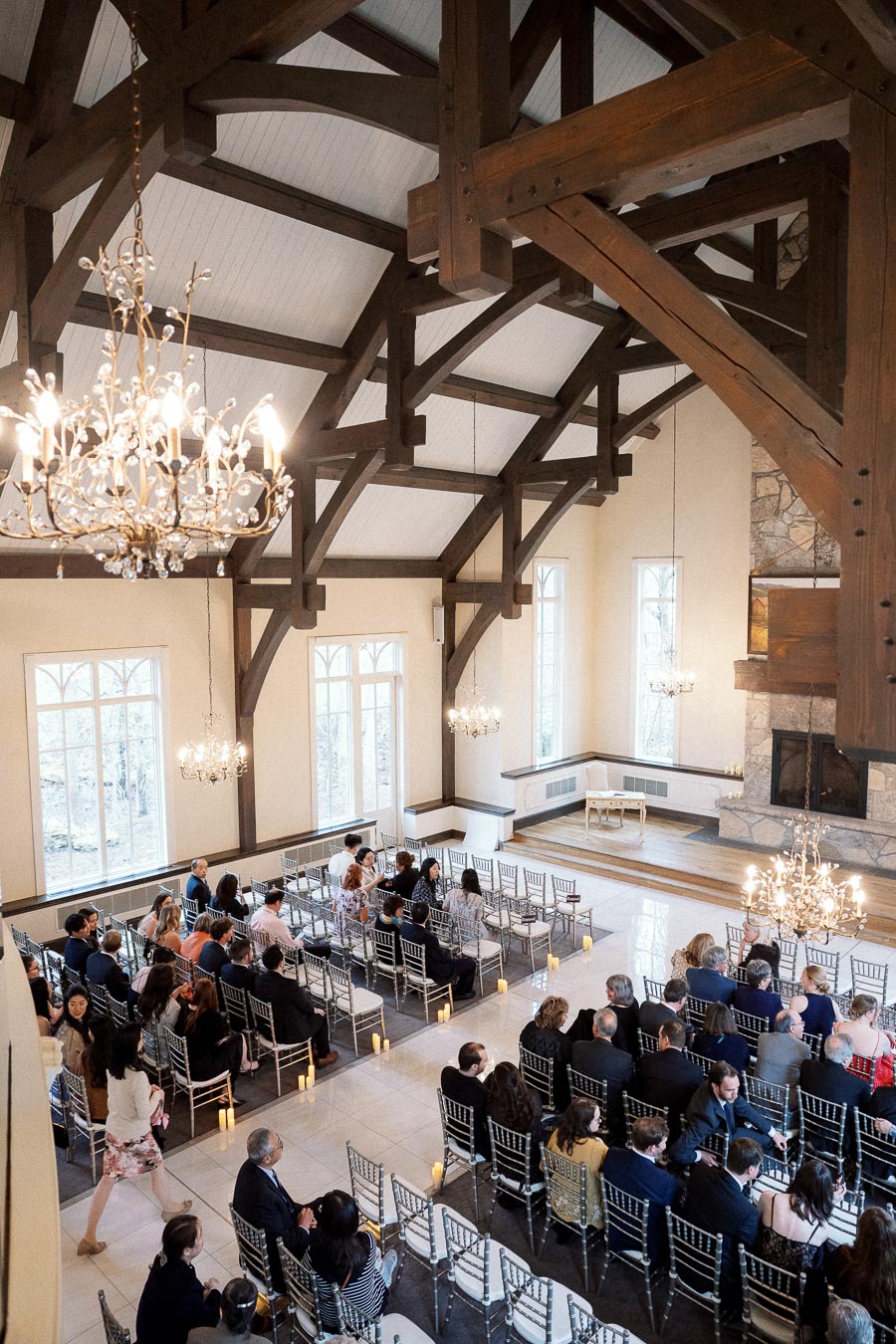 Guests seated in an elegant timber-framed hall with chandeliers and ceremony chairs