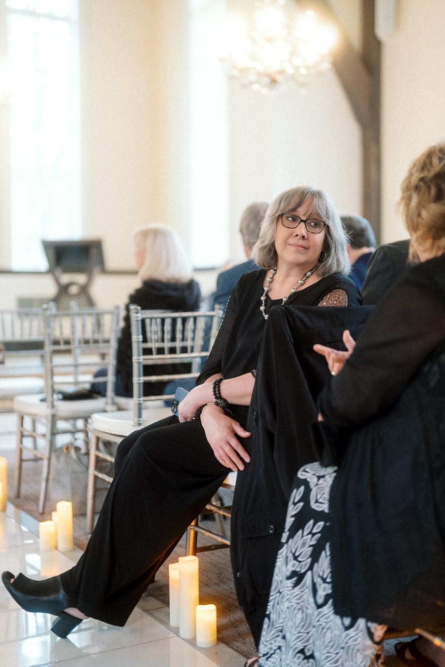 Woman in black seated among chairs and candles at an indoor event
