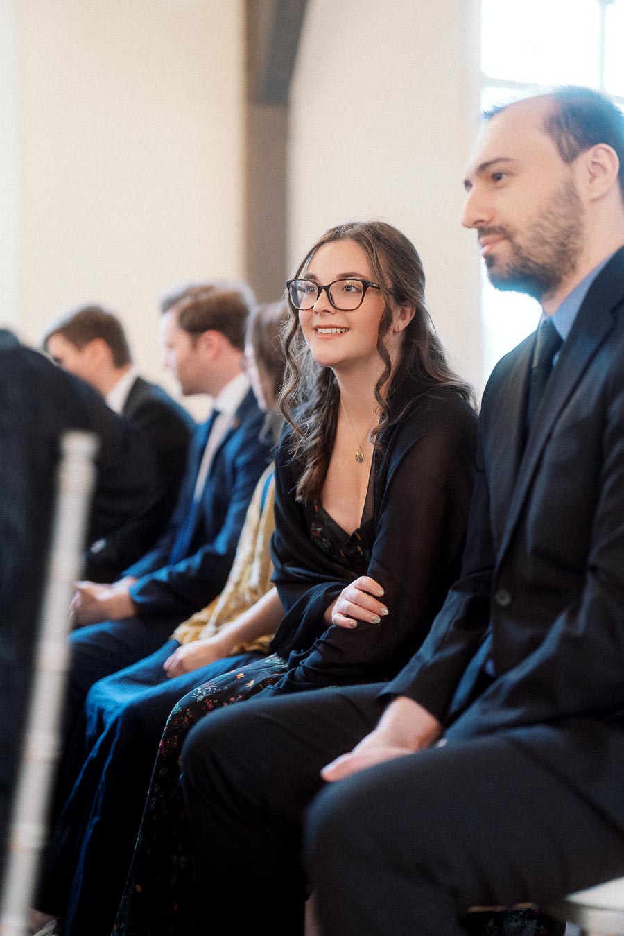 Well-dressed couple seated together among guests during an indoor ceremony