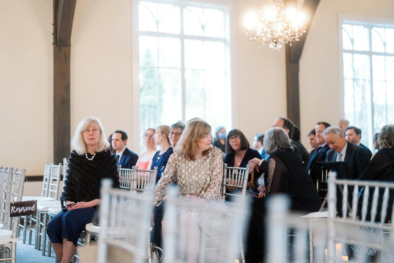 Guests seated in white chairs inside a bright ceremony room with large windows