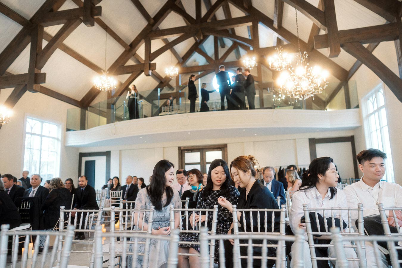 Guests seated in a bright timber-framed event hall with chandeliers and balcony