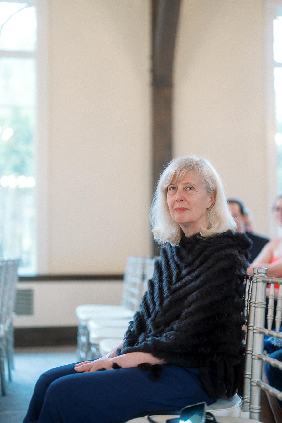 Woman in a black wrap seated on a silver chair indoors