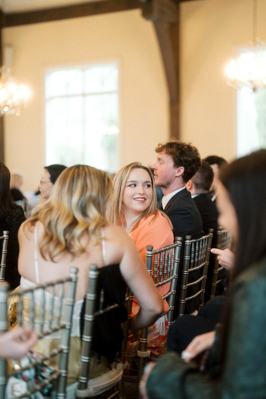 Guests seated on chiavari chairs converse inside a bright event hall.