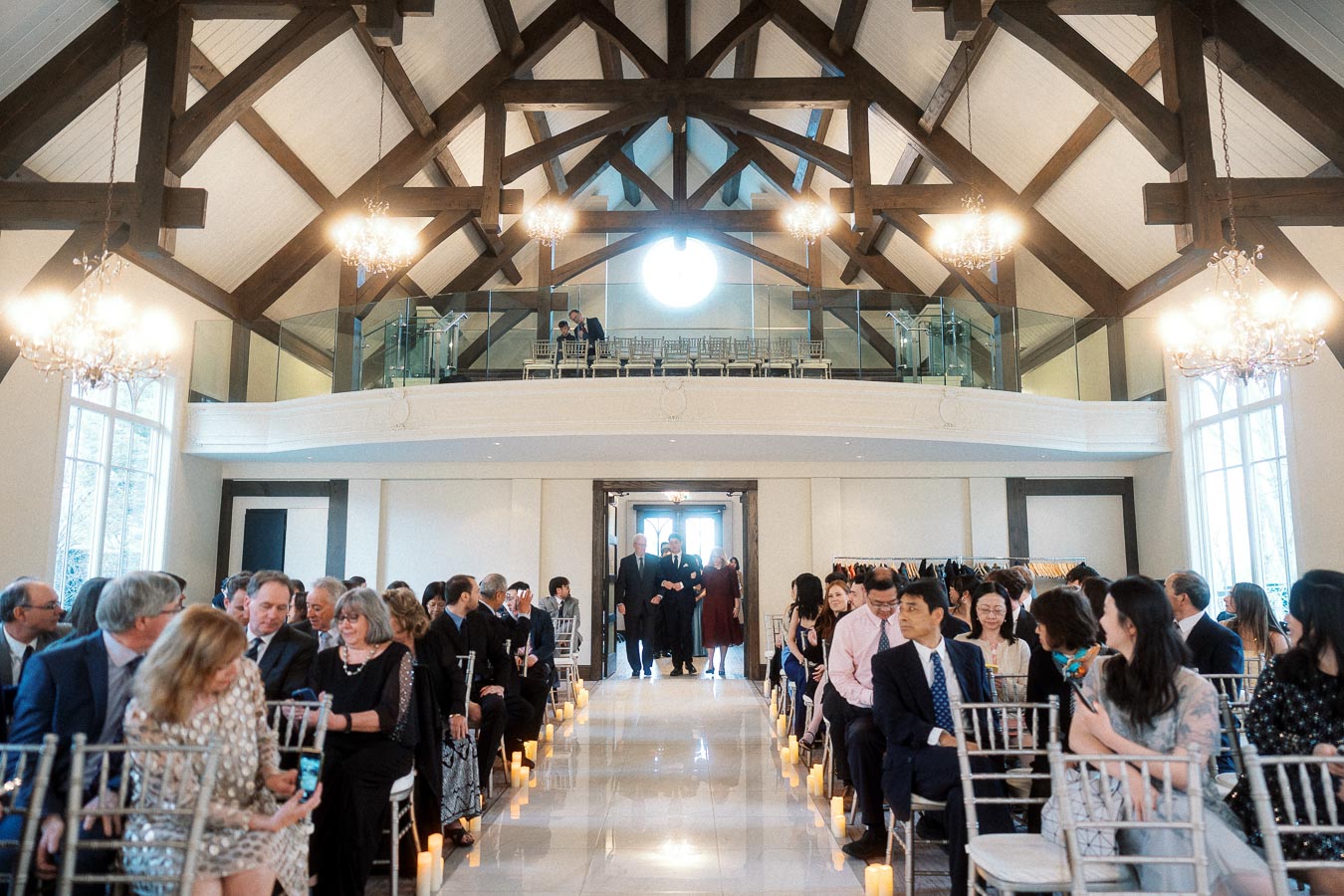 Wedding guests seated along an aisle inside a bright chapel with chandeliers