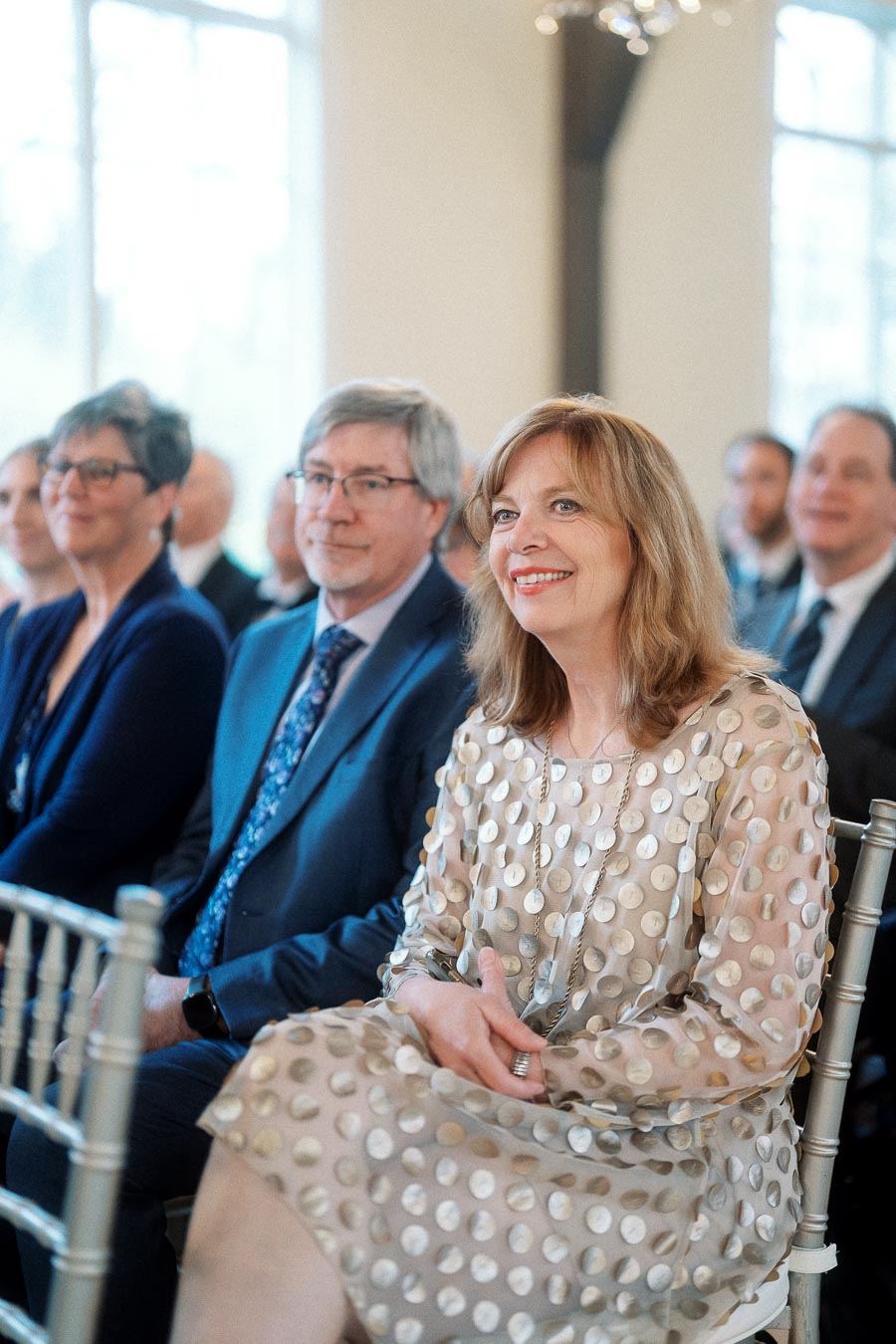 Guests seated indoors, smiling and watching a ceremony or event