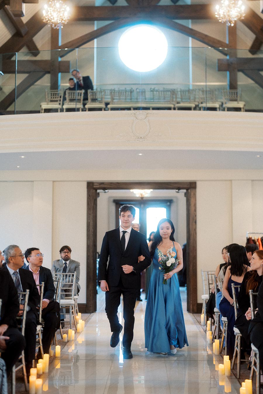 Formally dressed couple walking arm in arm down a candlelit ceremony aisle.