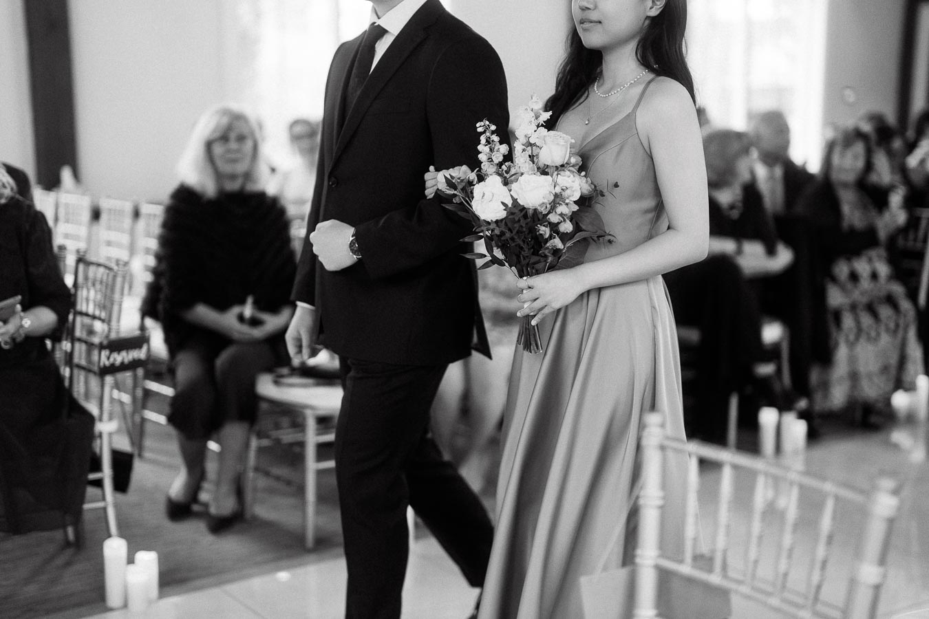 Couple walking down an indoor ceremony aisle, with the woman holding a bouquet.