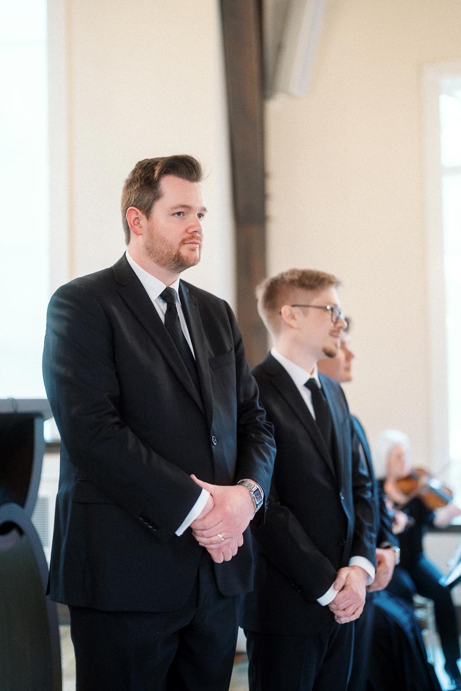 Two men in black suits standing indoors during a formal ceremony