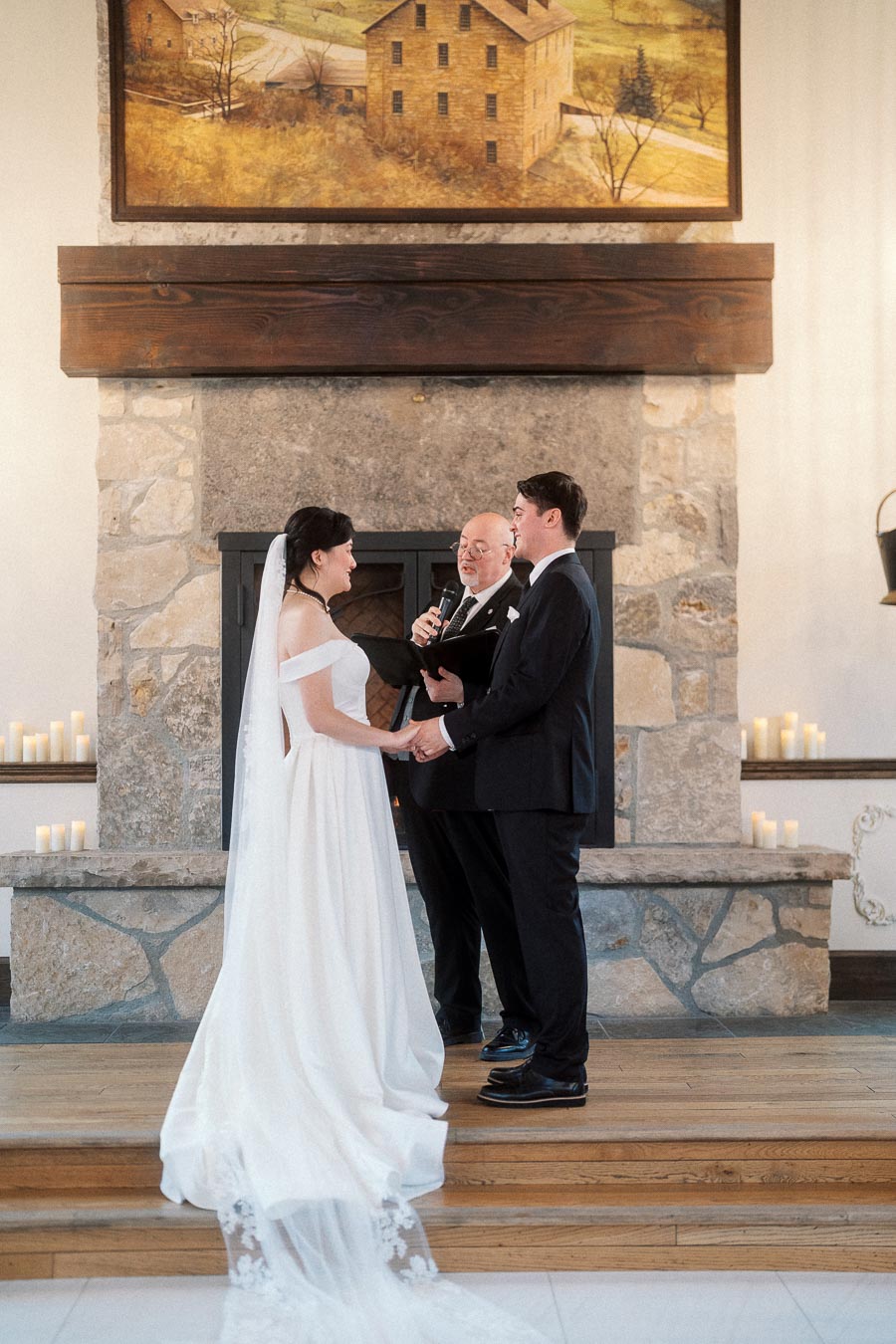Couple holding hands during an indoor wedding ceremony by a stone fireplace