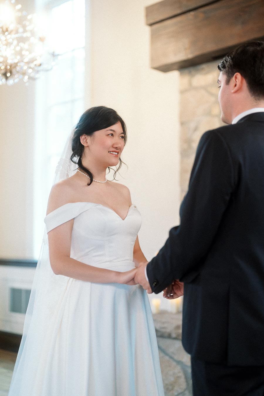 Couple in wedding attire holding hands indoors beside a stone fireplace.
