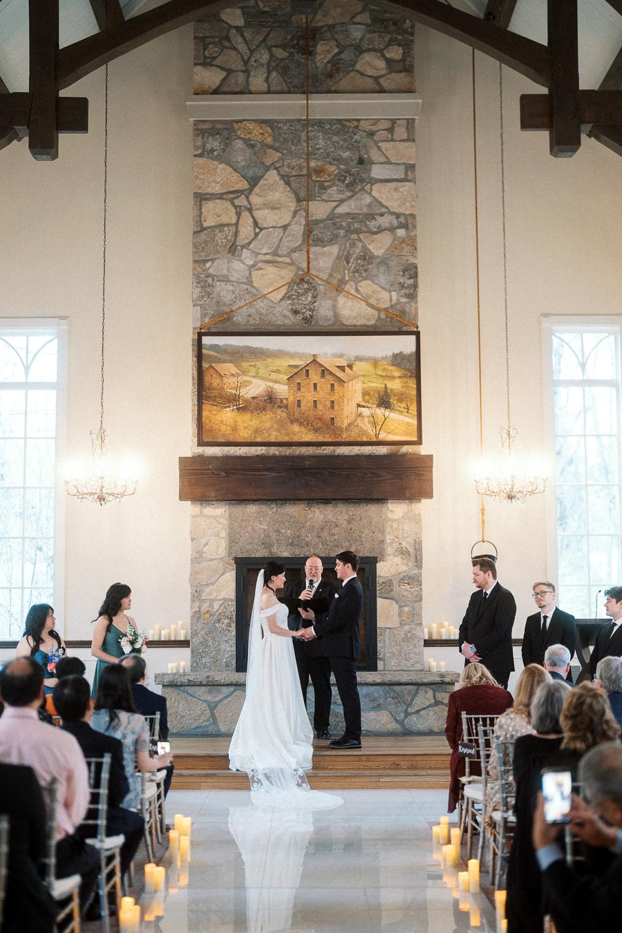 Couple standing at an indoor wedding ceremony in front of a stone fireplace.