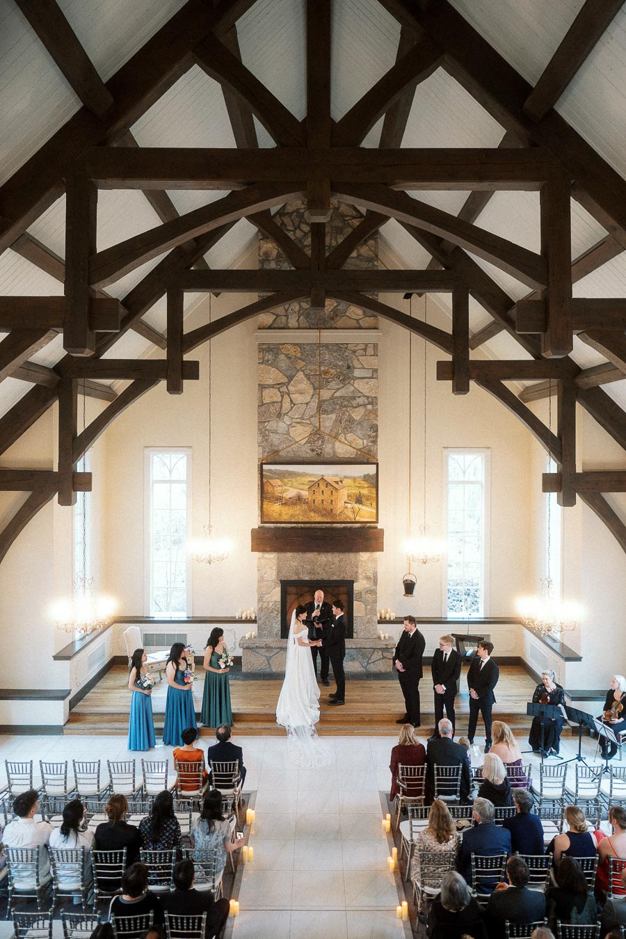 Indoor wedding ceremony beneath exposed wooden beams and a stone fireplace