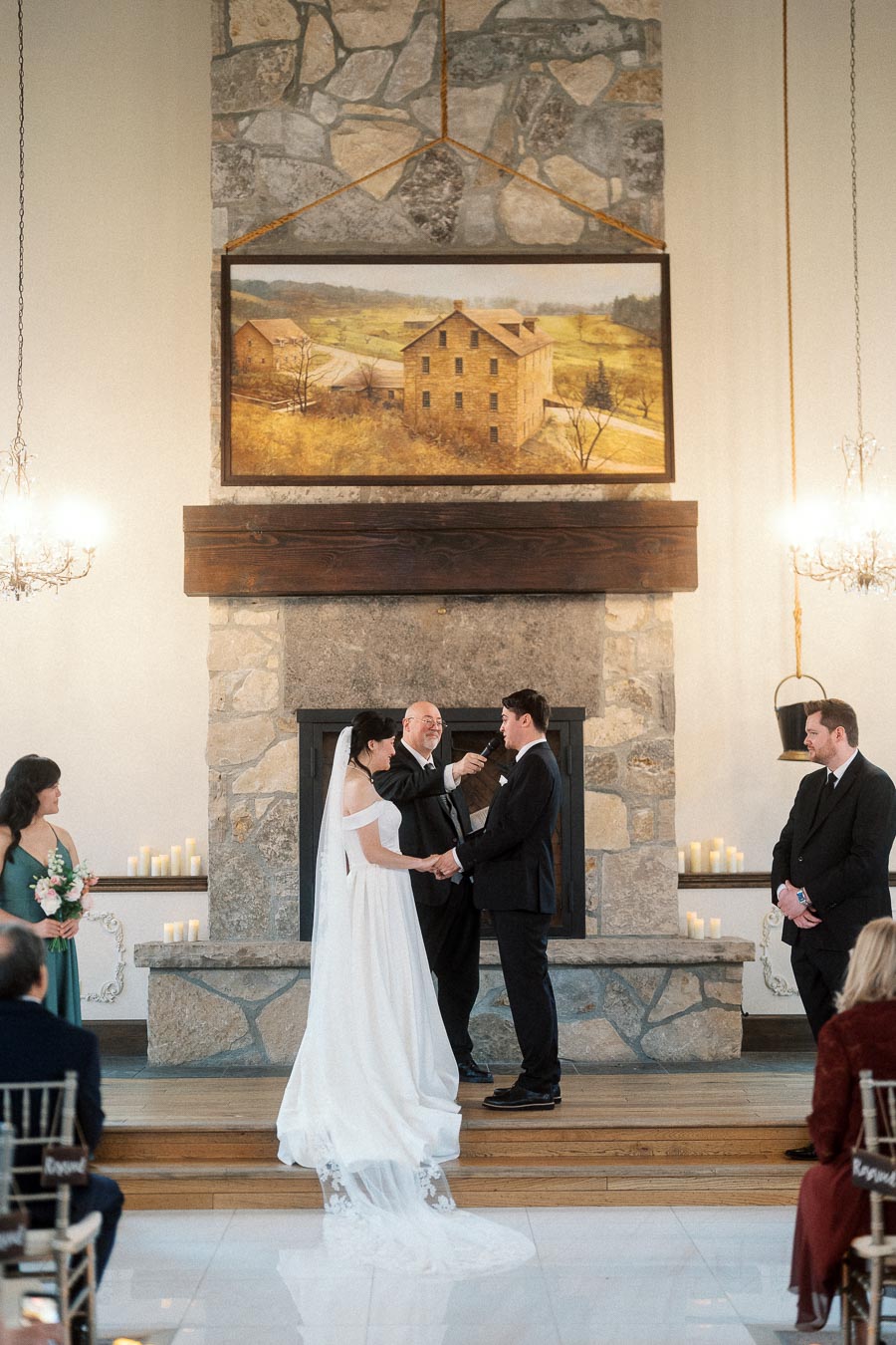 Couple holding hands during an indoor wedding ceremony before a stone fireplace