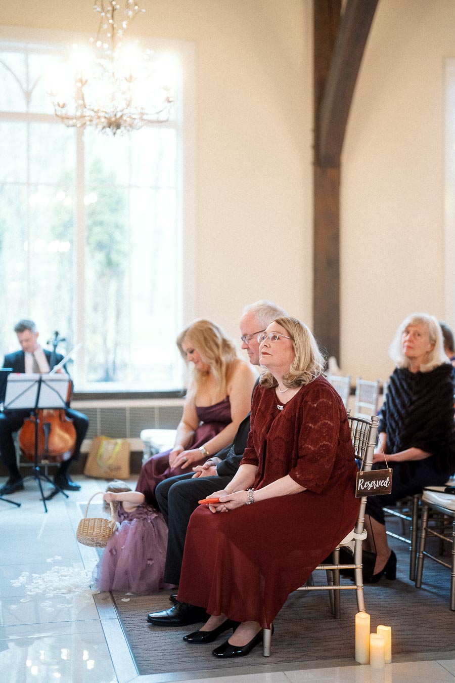 Seated guests listening indoors beside a reserved chair and live cellist