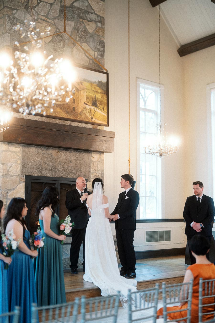 Couple exchanging vows during an indoor wedding ceremony by a stone fireplace.