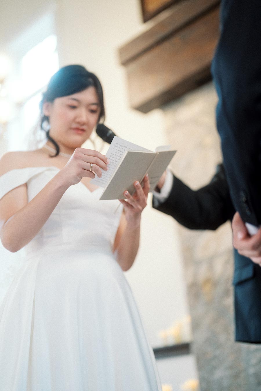 Woman in a white dress reads from a card beside a man holding a microphone.
