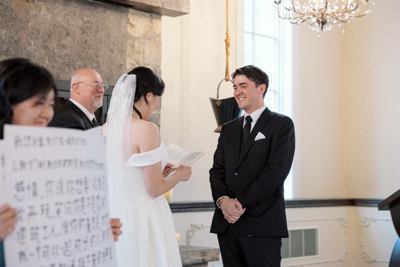 Bride reads vows to smiling groom during an indoor wedding ceremony.