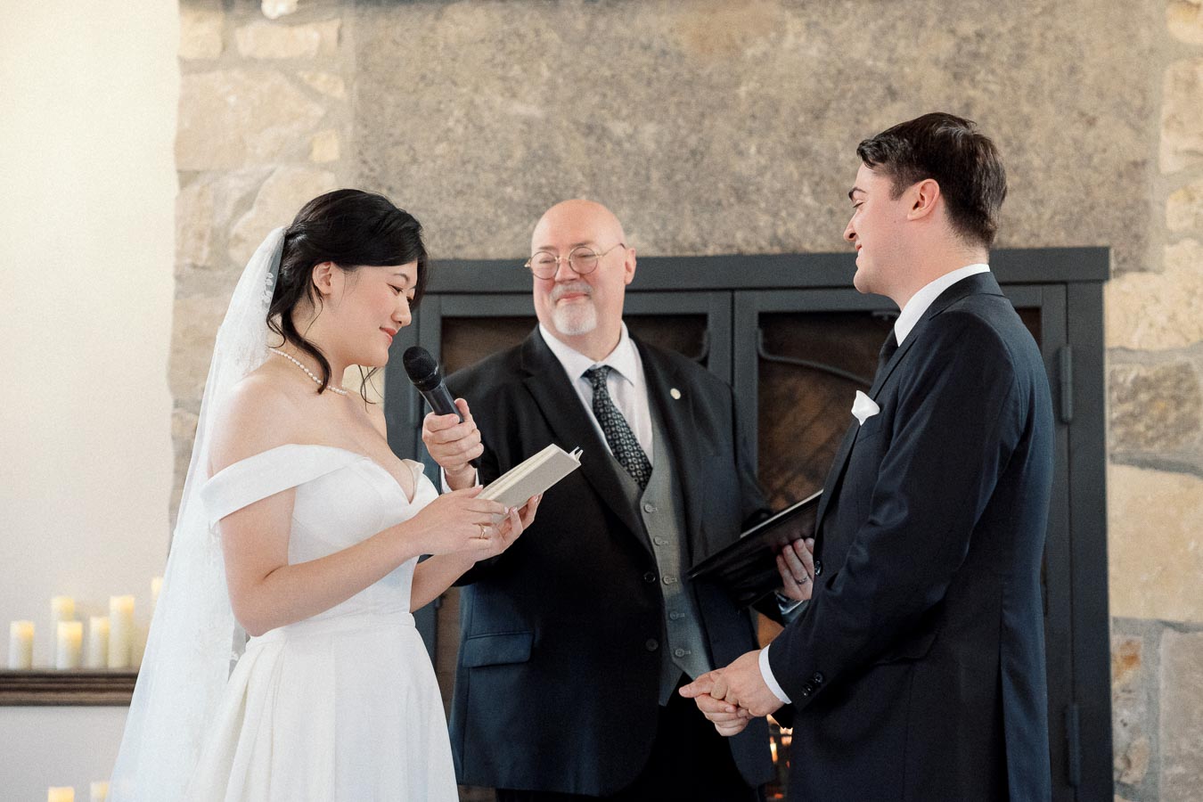 Bride reads vows to groom while an officiant holds a microphone.