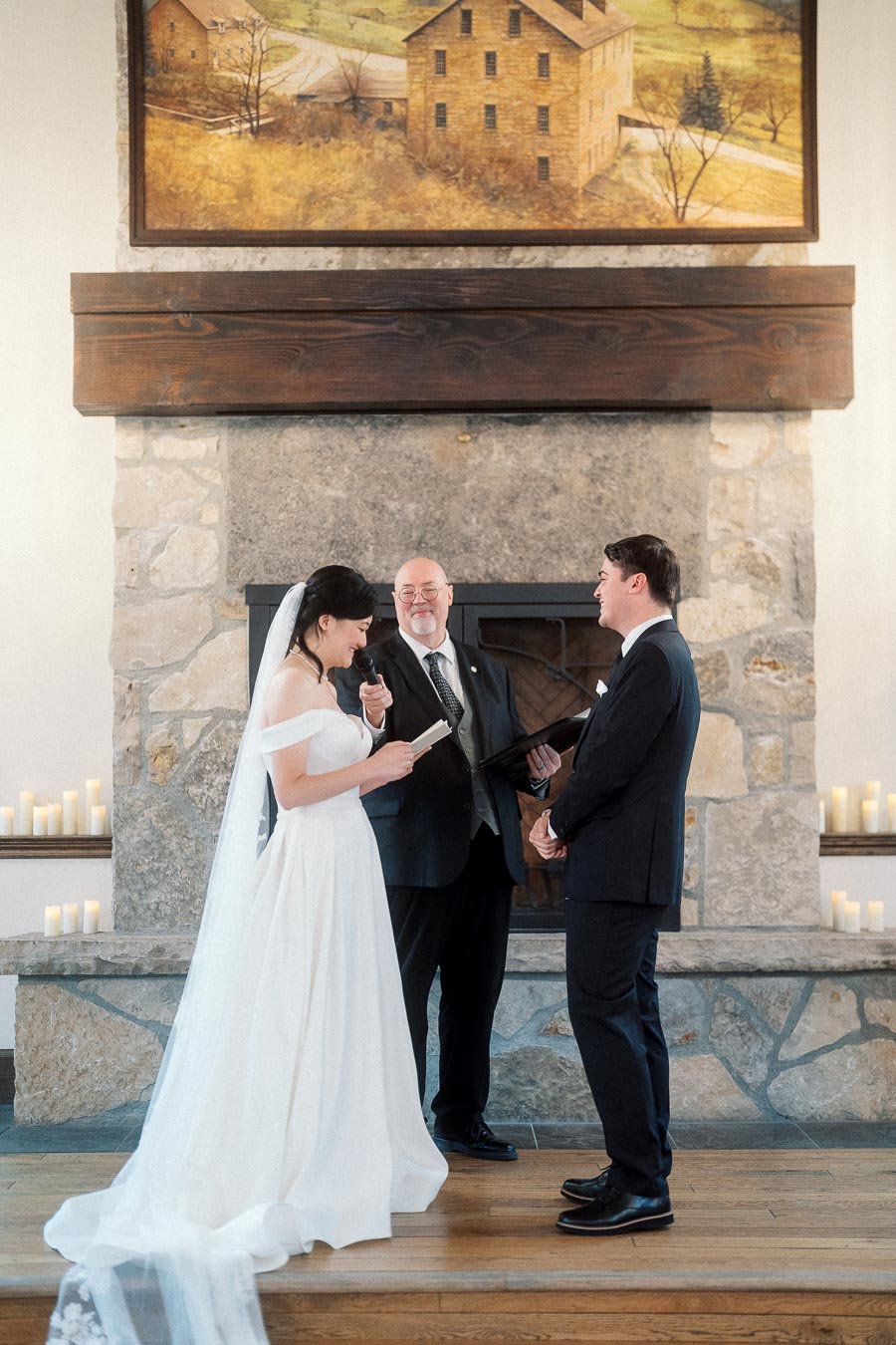 Bride reads vows to groom during an indoor ceremony beside a stone fireplace
