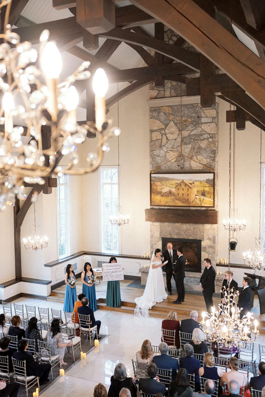 Couple exchanging vows during an indoor ceremony with guests seated beneath chandeliers.