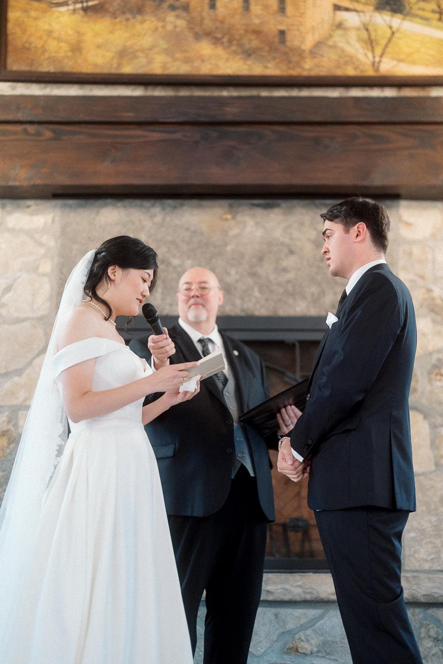Bride reads vows into a microphone as the groom and officiant listen.