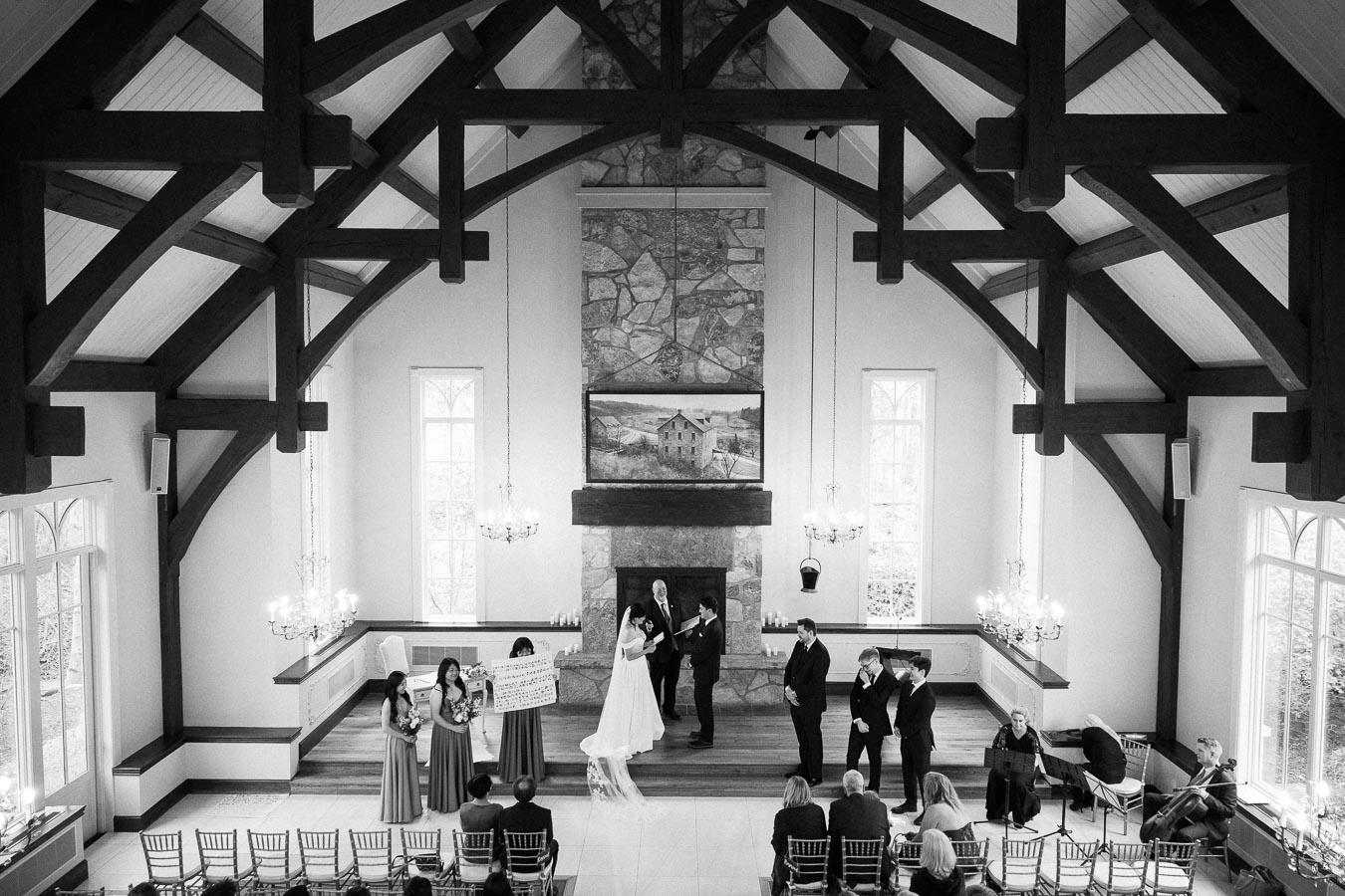 Black-and-white view of a wedding ceremony inside a chapel with timber beams.