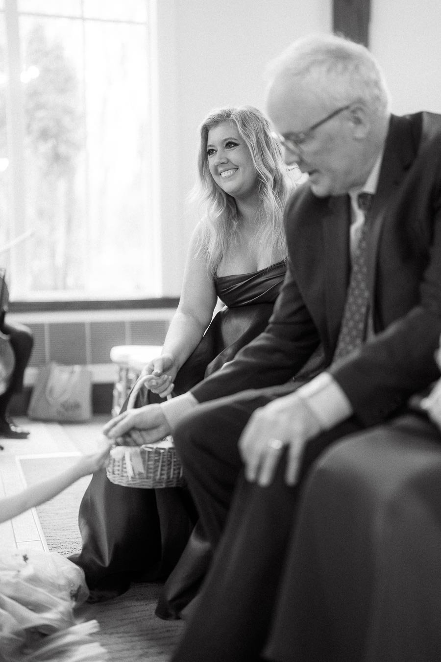 Woman in formal dress smiles while seated beside an older man indoors