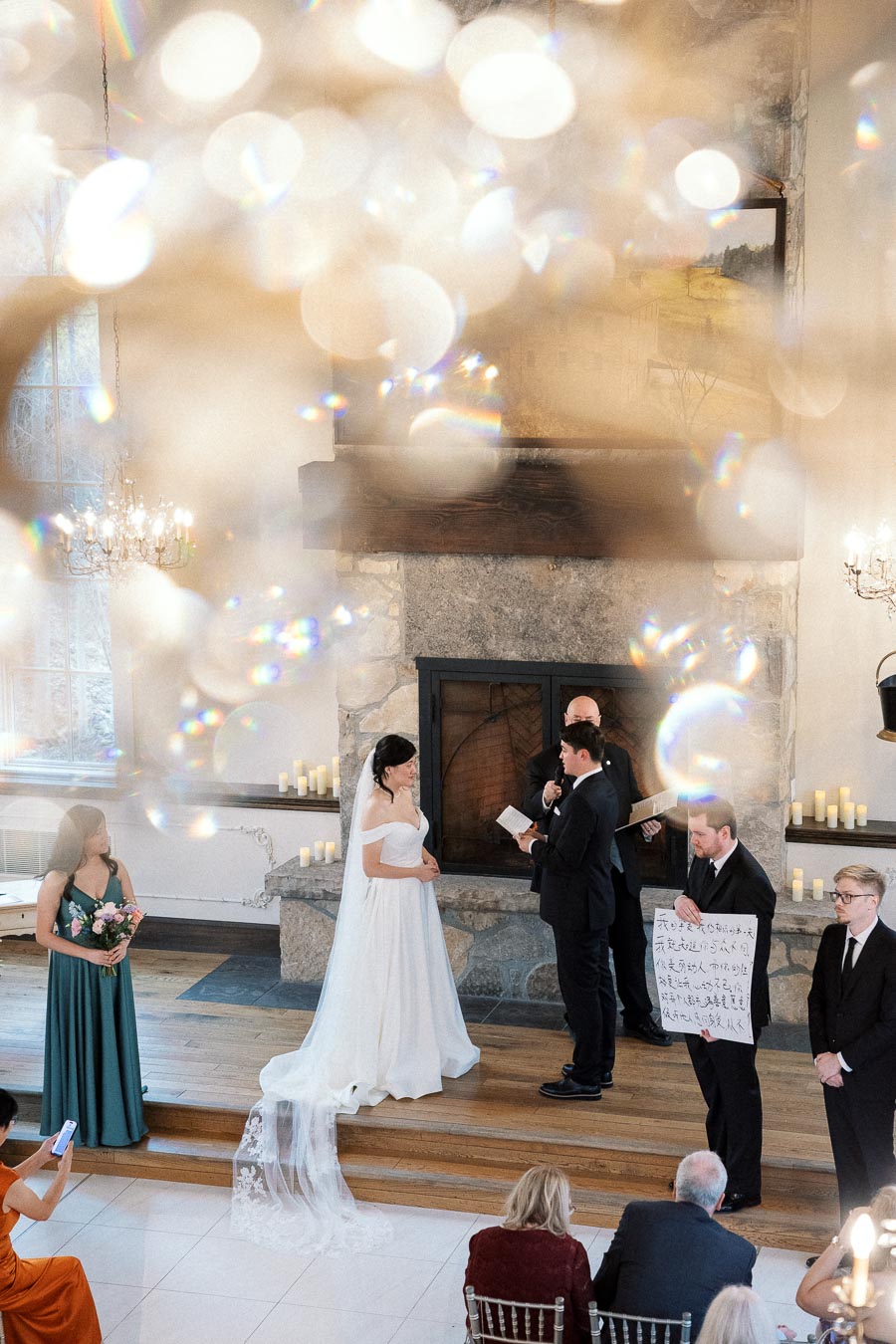 Bride and groom exchange vows during an indoor wedding ceremony by a stone fireplace.