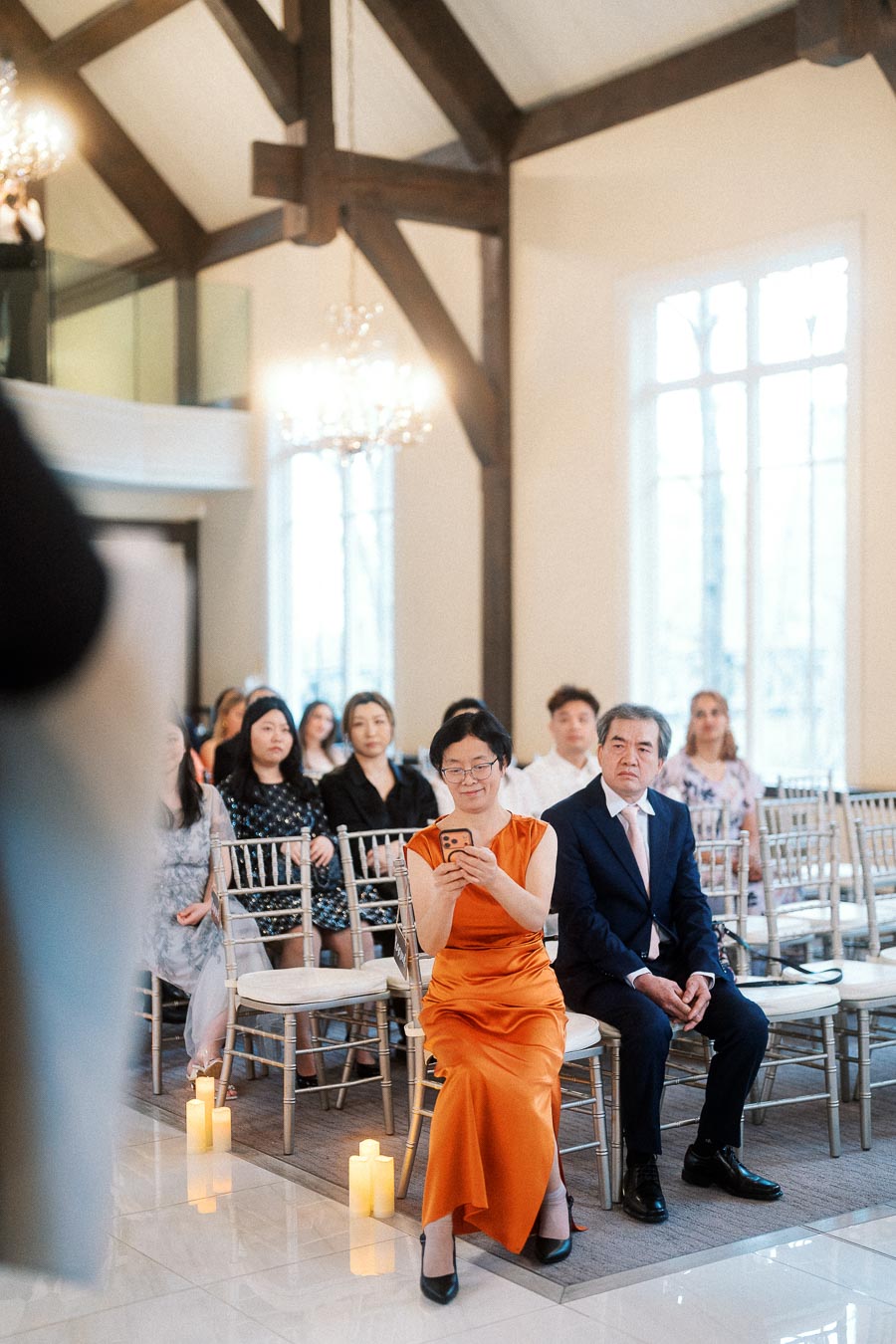 Guests seated in an elegant ceremony room, with one woman holding up a phone