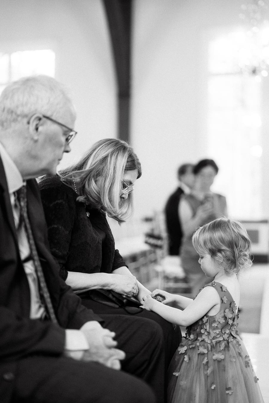 Young flower girl interacts with seated guests during an indoor ceremony.