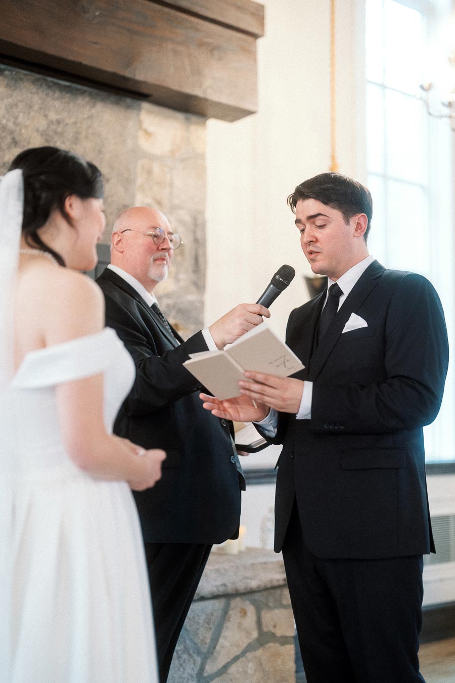 Groom reads vows into a microphone during an indoor wedding ceremony.