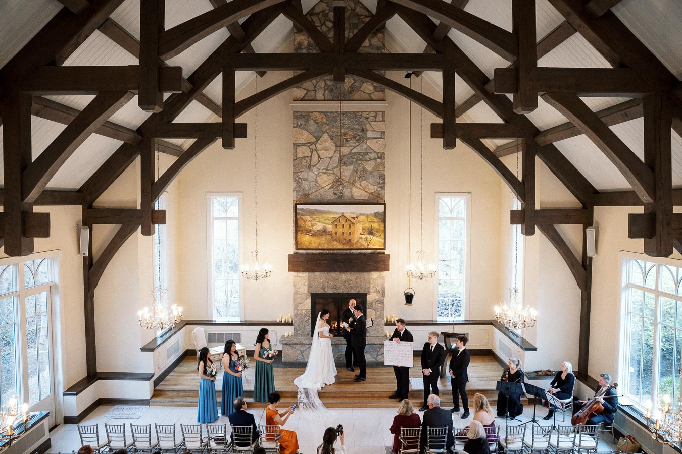 Couple exchanging vows in a chapel with timber beams, chandeliers, and seated guests.