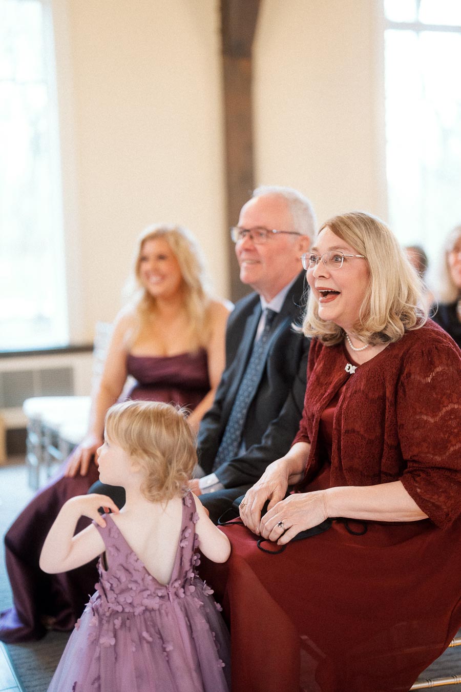 Guests seated indoors react warmly as a young child stands nearby.