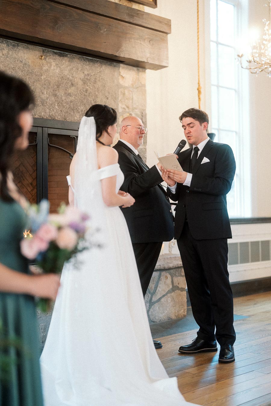 Groom reads vows during an indoor wedding ceremony beside the bride and officiant.