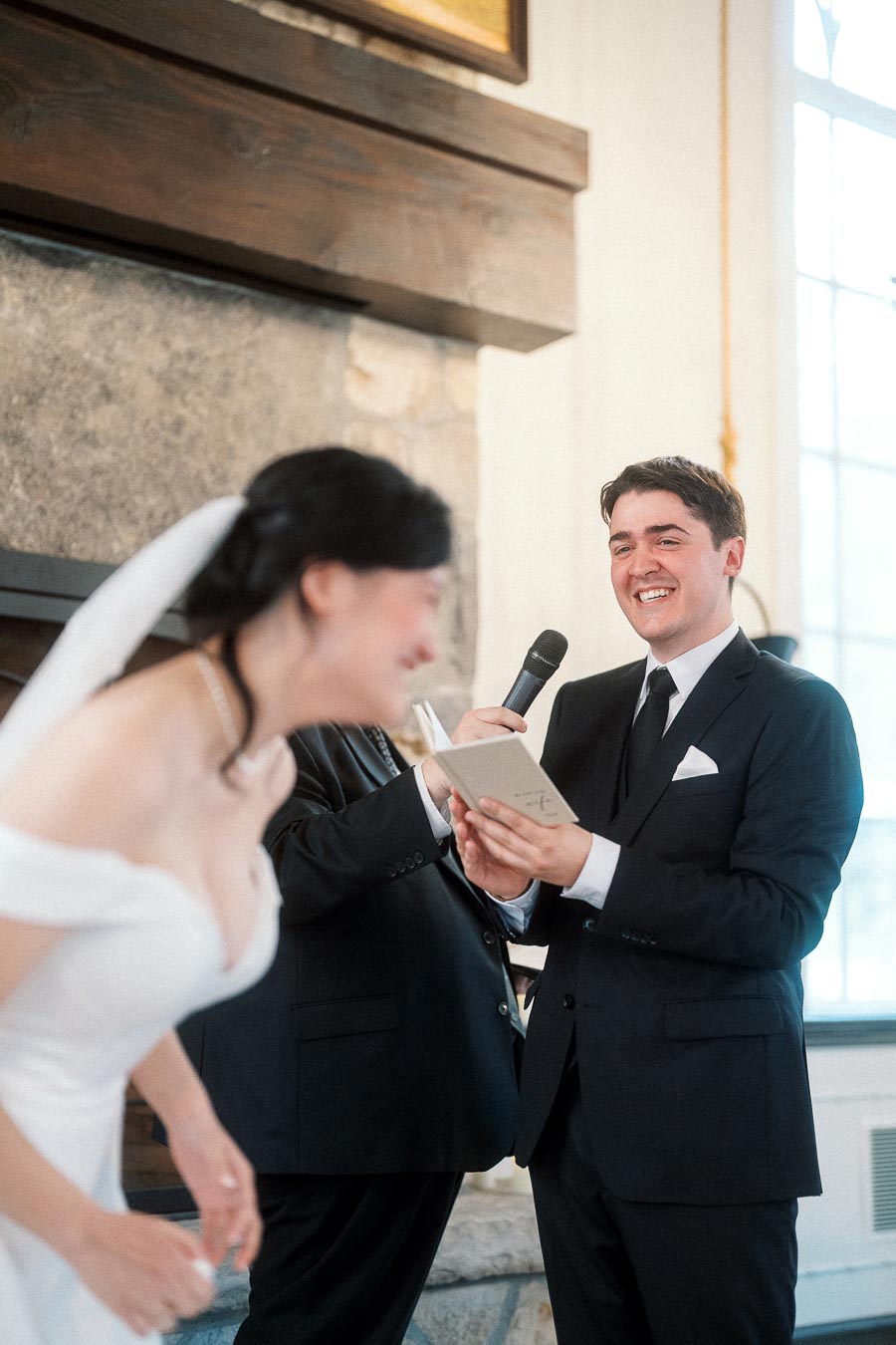 Groom smiling while reading vows as bride laughs during an indoor ceremony