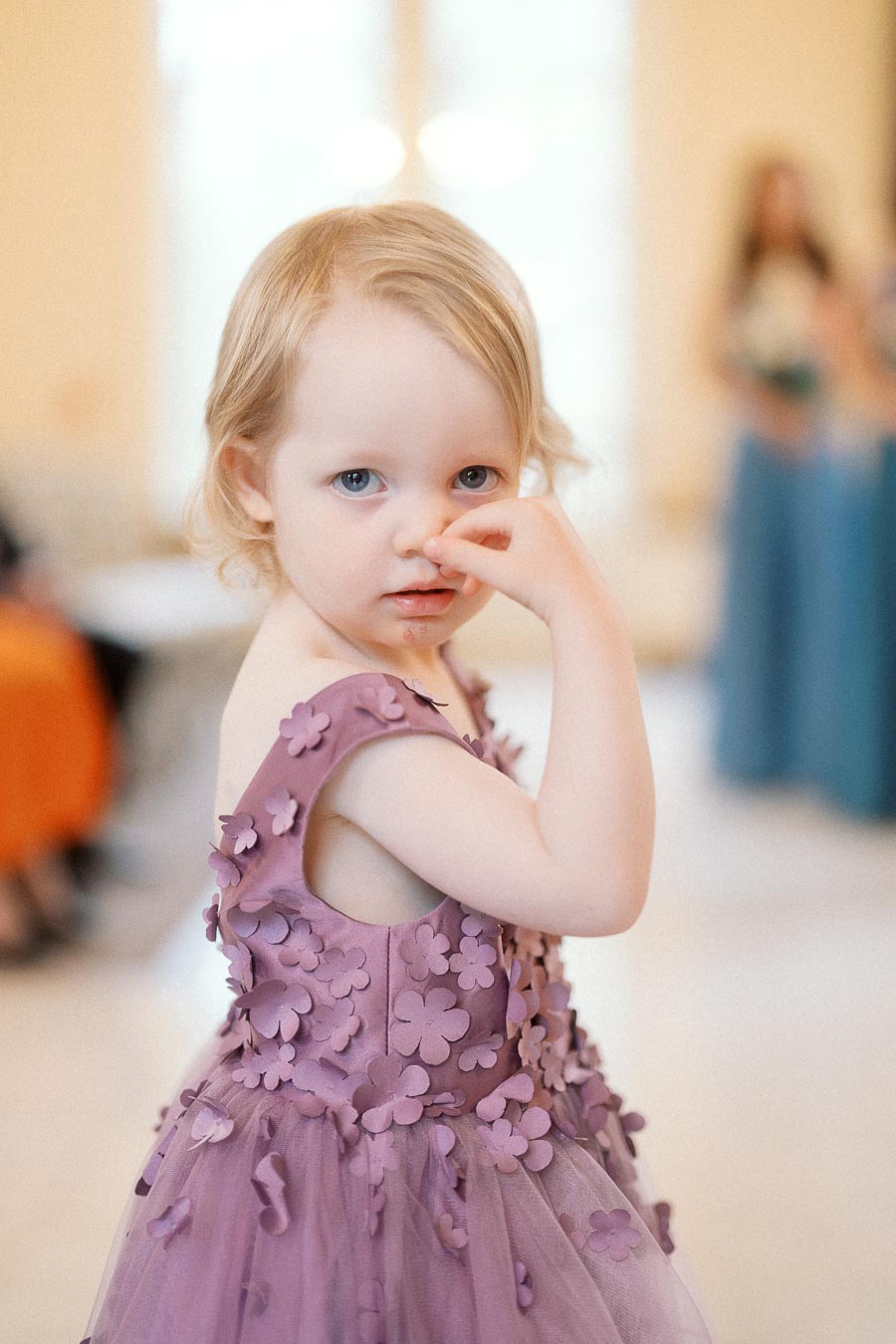 Young child in a lavender floral dress looking at the camera indoors