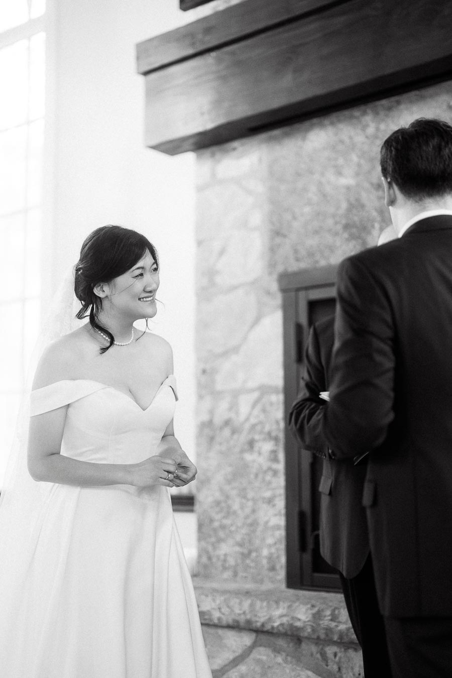 Smiling bride in an off-shoulder gown facing a suited partner indoors