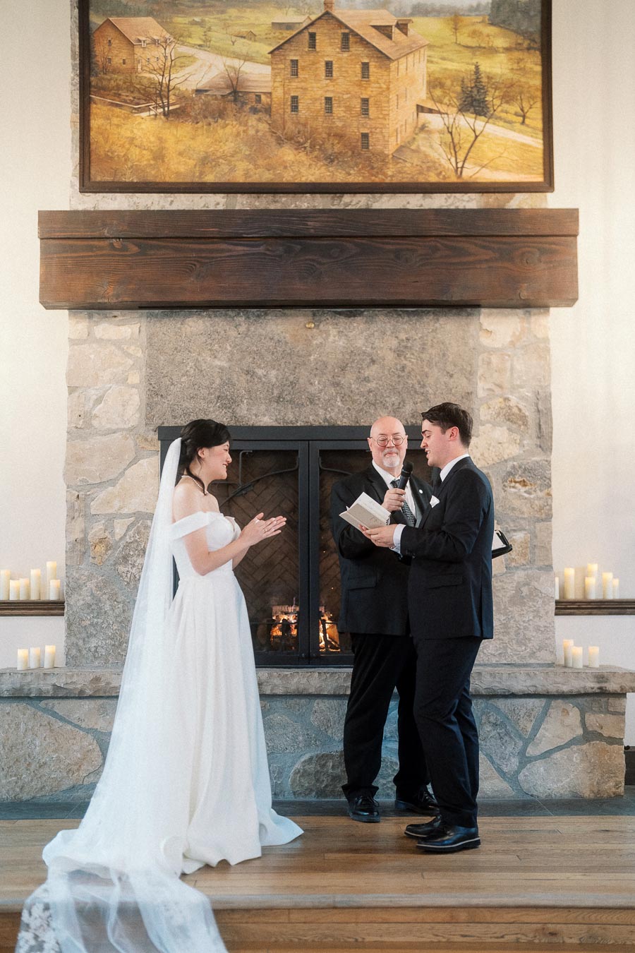 Couple exchanging vows with an officiant in front of a stone fireplace.