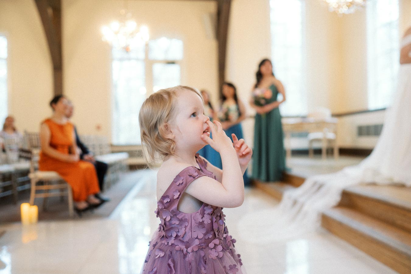 Young child in a purple dress watching a wedding ceremony indoors
