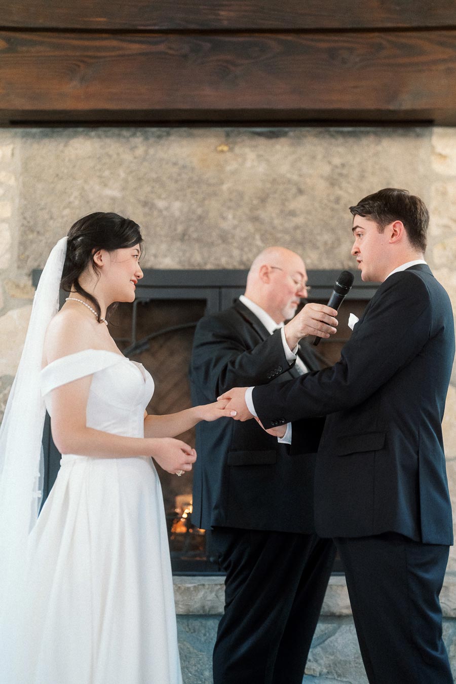 Bride and groom hold hands during an indoor wedding ceremony by a fireplace