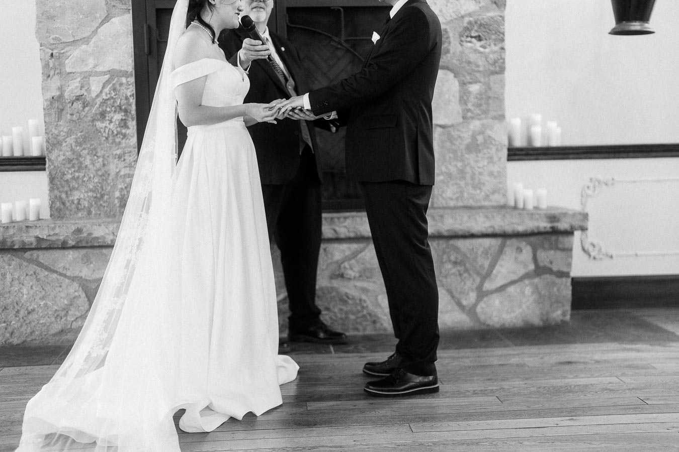 Couple holding hands during an indoor wedding ceremony by a stone fireplace