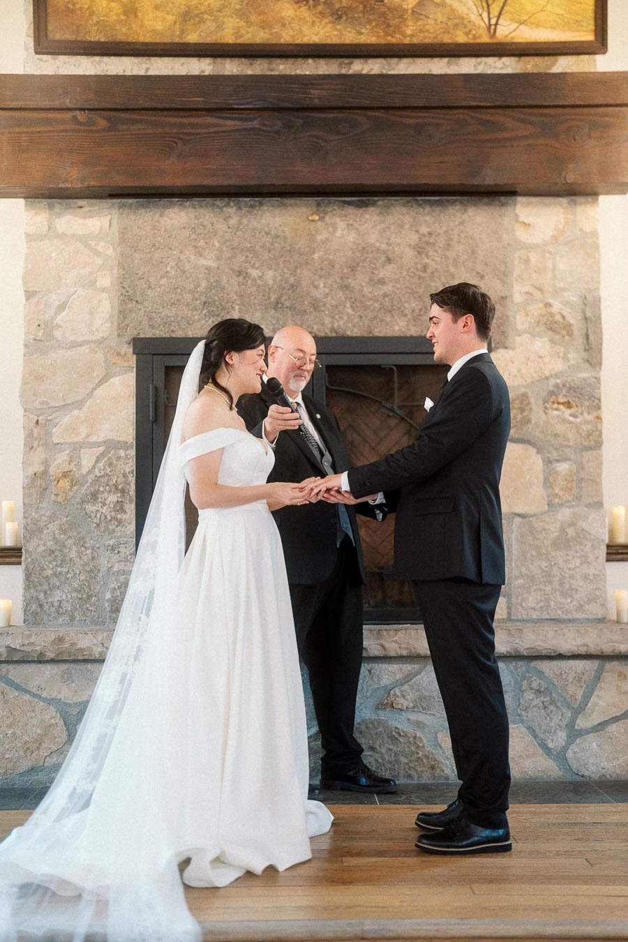 Couple exchanging vows during an indoor ceremony in front of a stone fireplace