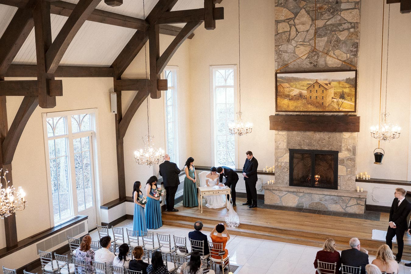 Couple signing documents during an indoor ceremony in a vaulted hall.